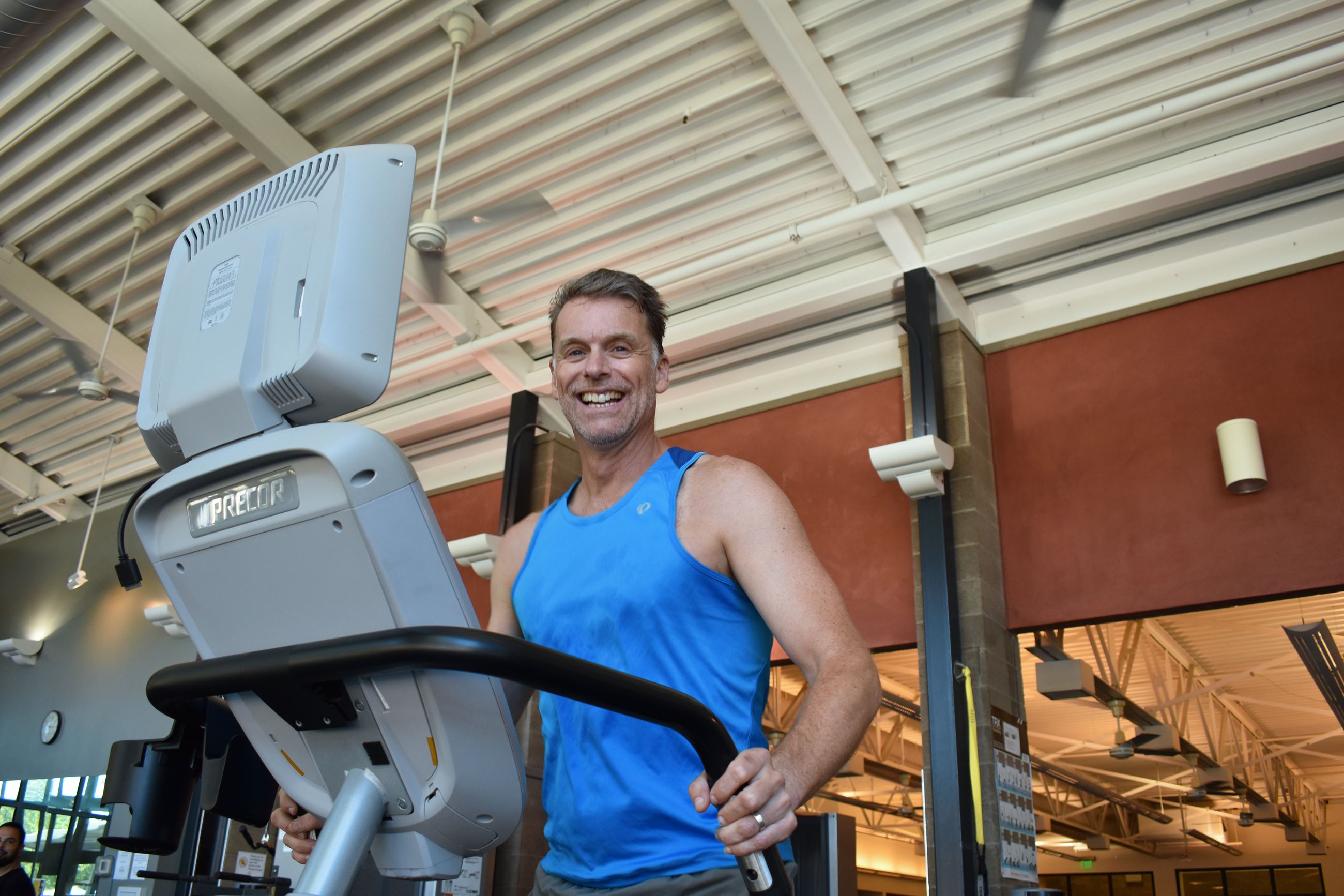 Man in blue sleeveless shirt smiling while running on treadmill at CRC